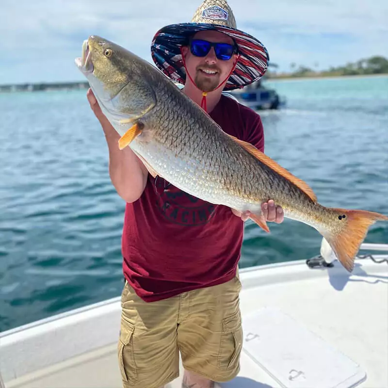 man with sunglasses and a hat holding a fish on a boat